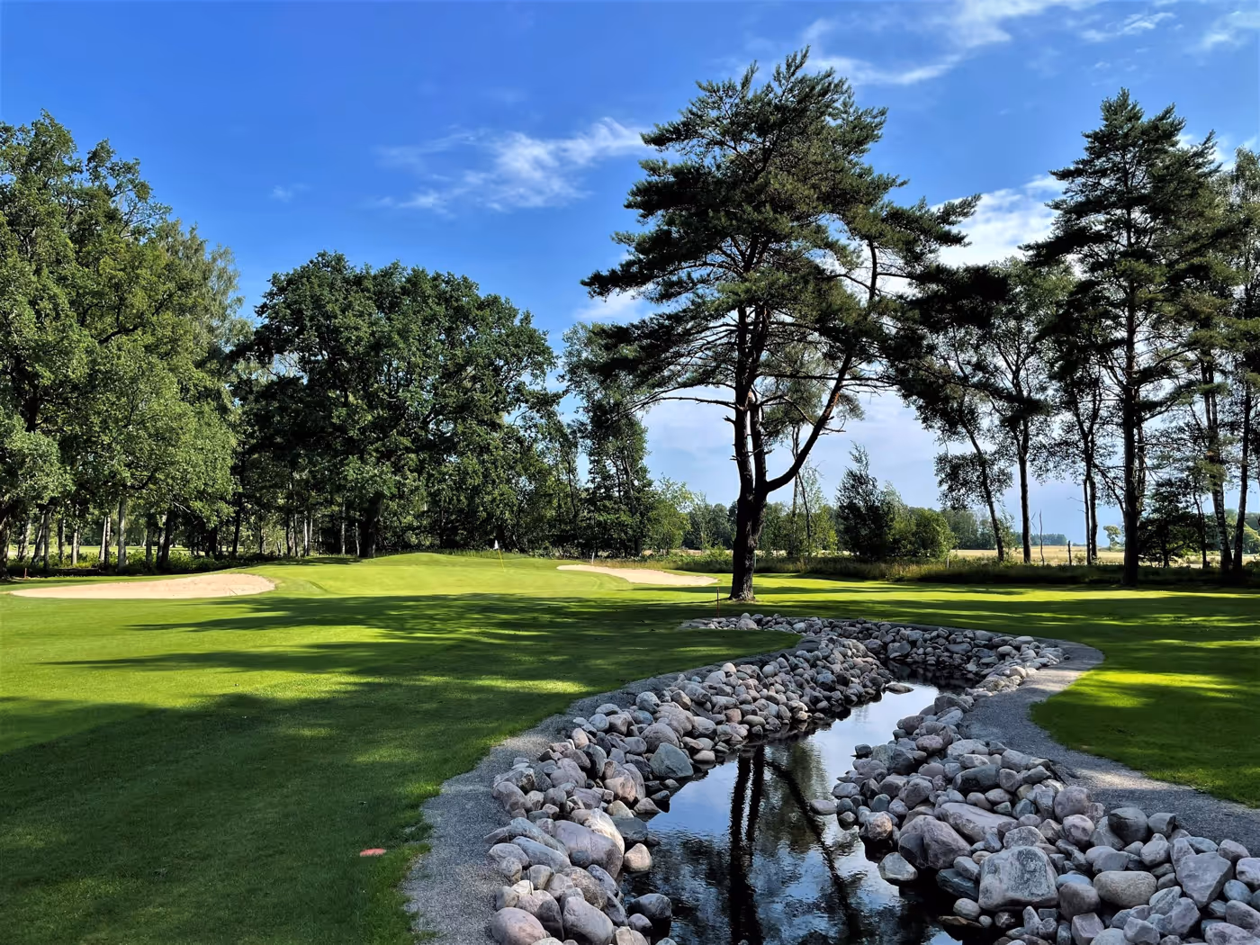 Närliggande golfbana med damm, bunker och skogslandskap